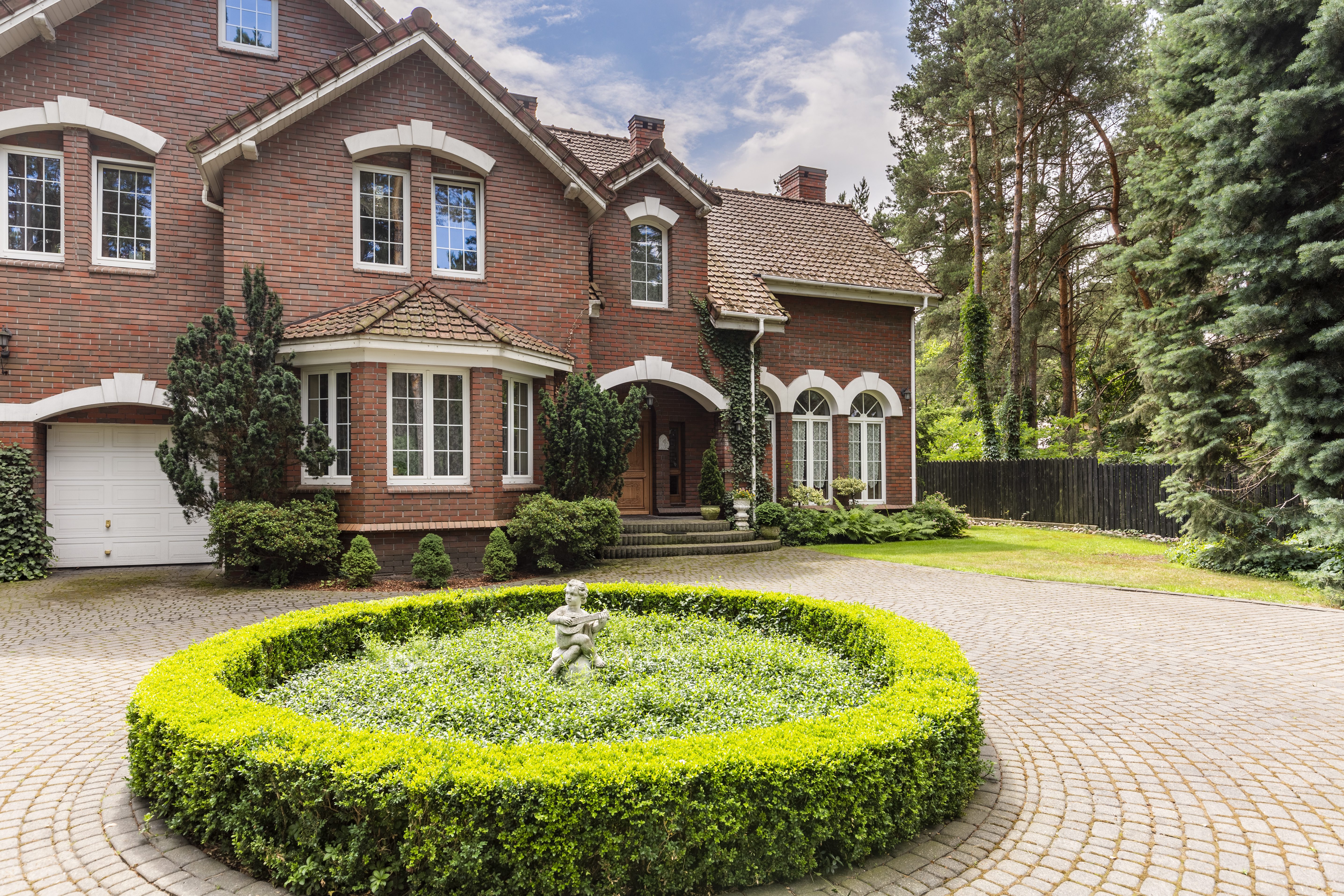 Round hedge and a small statue in the middle of a cobblestone dr